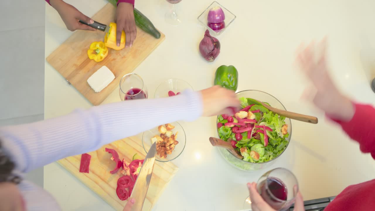 Diverse female cooks preparing fresh salad slicing peppers in kitchen while tossing greens