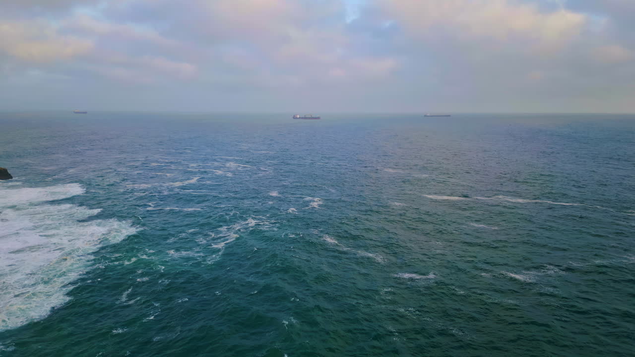 추운 회색의 바다가 무거운 구름이 가득한 하늘 아래에서 파동하고, 멀리 떠다니는 배.