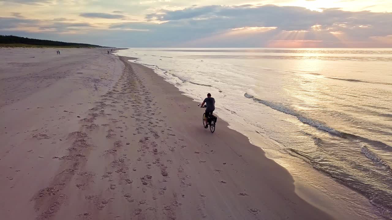 Ripresa al rallentatore di un giovane uomo in bicicletta sulla spiaggia al tramonto
