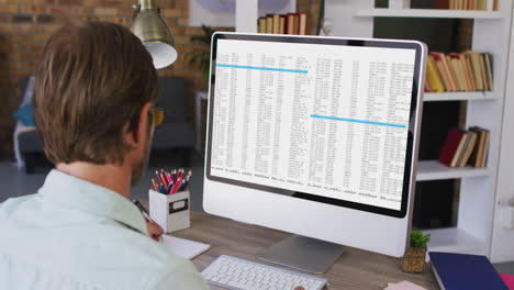 caucasian man sitting at desk watching coding data processing on computer screen