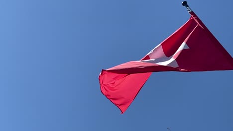 A-red-and-white-Swiss-flag-flies-in-the-blue-summer-sky-in-slow-motion