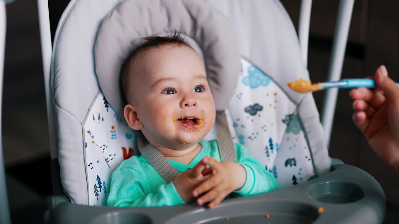 Happy baby during feeding. Kid laughs and waves hands cheerfully while mom nourishes him.