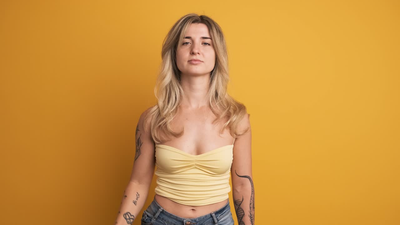 Unhappy young woman pointing thumb down disapprovingly on yellow background