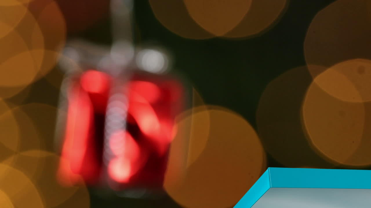 Animation of red present christmas bauble decoration over orange spots of light