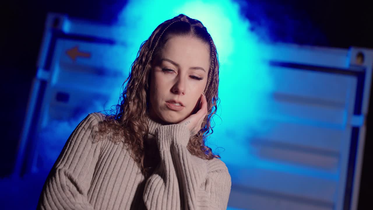 Cinematic low-angle portrait of a woman standing in blue smoke and fog at night, creating a dramatic, mysterious atmosphere. Concept for nightlife aesthetics, fashion mood, and dreamy cinematic