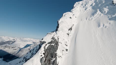 Summiting-snow-covered-mountain-peek-and-flying-down-in-FPV-drone-view