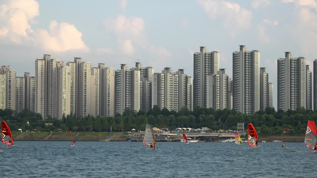 Due windsurfisti che sfrecciano sul fiume Han al tramonto, con gli appartamenti Jamsil sullo sfondo e bellissime nuvole rosate, a Seul, Corea del Sud.