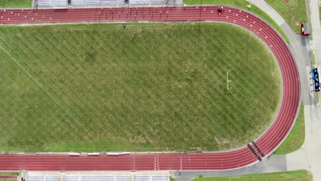 top down aerial birds eye view of red track, green athletic field, student athletes practicing