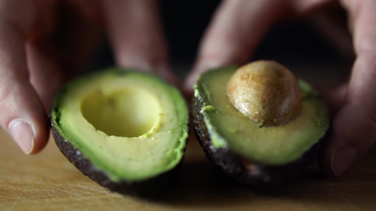mani del maschio caucasico che spingono l'avocado verde dimezzato verso la telecamera sul tagliere di legno