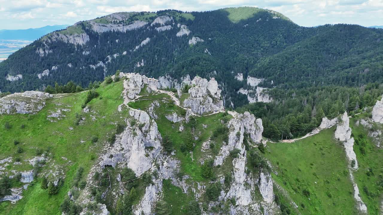 Aerial orbit drone footage captures a rugged rocky ridge surrounded by green alpine slopes and dense forests, highlighting the dramatic landscape and hiking trails. Location: Mala Fatra, Slovakia