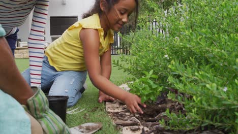 Niña-Hispana-Con-Padres-Aprendiendo-A-Plantar-Flores-En-El-Jardín.