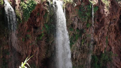 slow-motion view of upper ouzoud waterfalls cascading down mossy cliffs with scattered green vegetation.