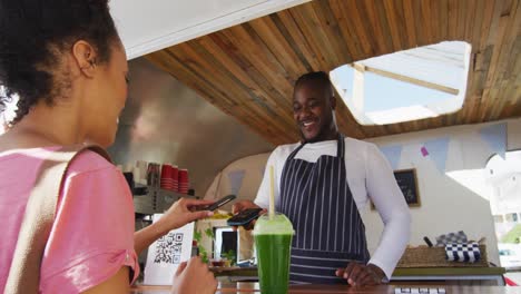 cliente feliz mujer pagando sonriente afroamericano hombre dueño de camión de comida por teléfono inteligente