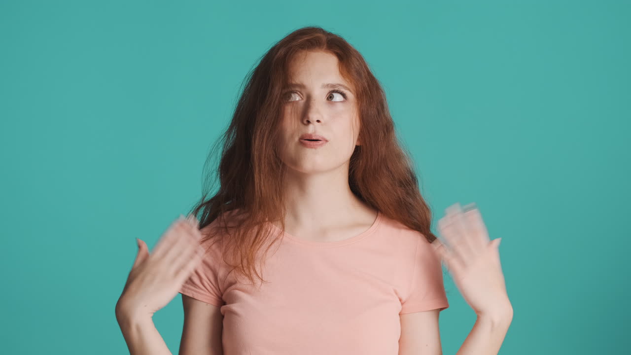 рыжая девушка смотрит в камеру на бирюзовом фоне.