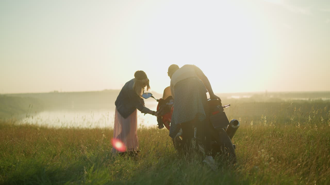 두 명의 여성이 배경에 흐릿한 물체 근처의 넓은 열린 잔디에서 빨간색 전력 자전거를 조심스럽게 청소하고 있습니다.