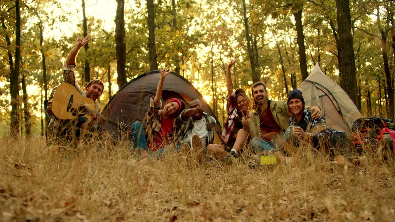 un grupo feliz de amigos exploradores durante una pausa de acampada toman una foto de grupo con ropa de senderismo contra el telón de fondo de las tiendas de campaña en un bosque verde-amarillo de otoño. foto y efecto flash