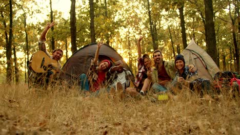 A-happy-group-of-scout-friends-during-a-camping-break-take-a-group-photo-in-hiking-clothes-against-the-backdrop-of-tents-in-an-autumn-green-yellow-forest.-Photo-and-flash-effect