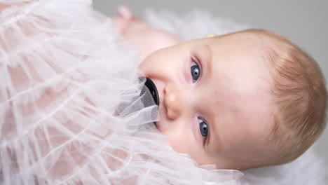 face of an adorable grey-eyed caucasian baby with pacifier. infant swayed in mom's hands falling asleep. close up.