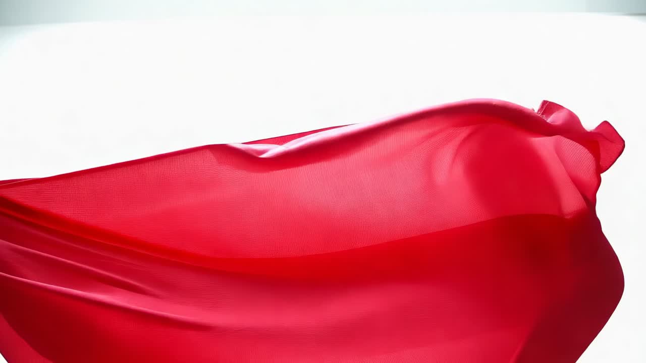 Tessuto di seta rosso ondeggiante, illuminato in controluce in studio da una ventola fuori campo, che rivela pieghe trasparenti