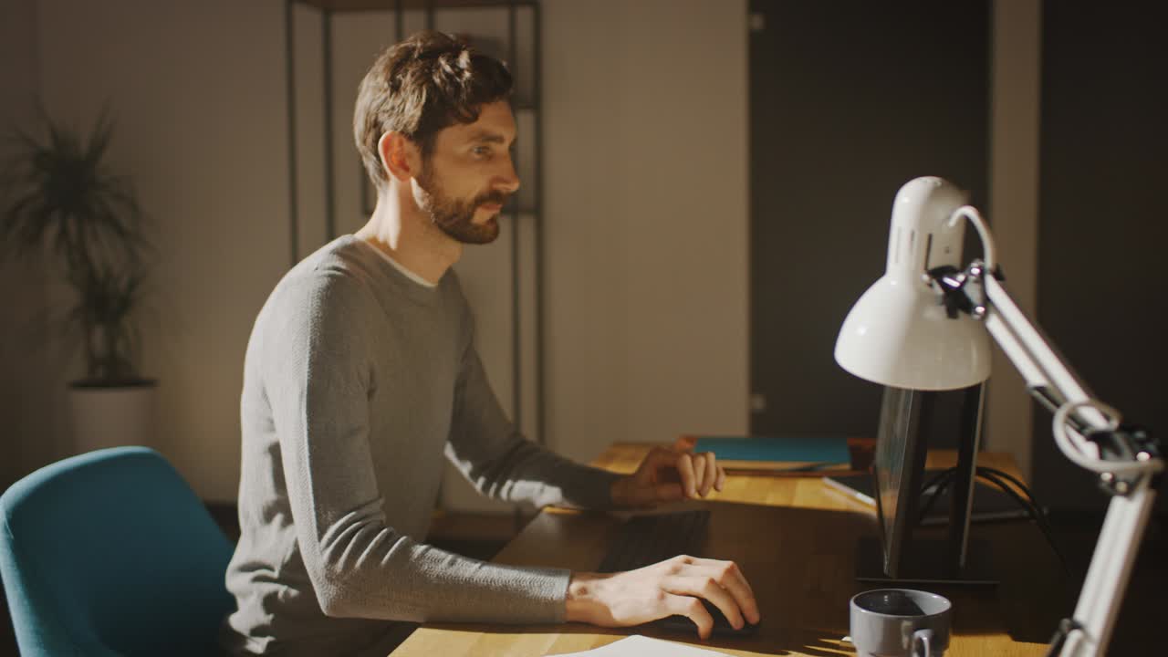 Designer seduto alla sua scrivania in uno studio ufficio, lavora su un computer desktop con un'applicazione di sviluppo software per smartphone sullo schermo. Movimento energico e veloce. Ripresa ad arco con tracking a 360 gradi.