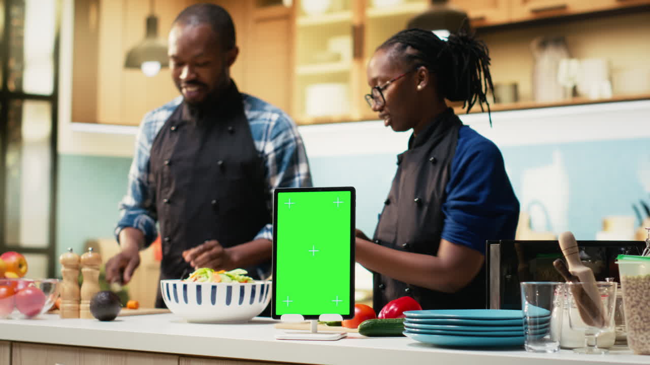 African American couple cooking in kitchen with tablet