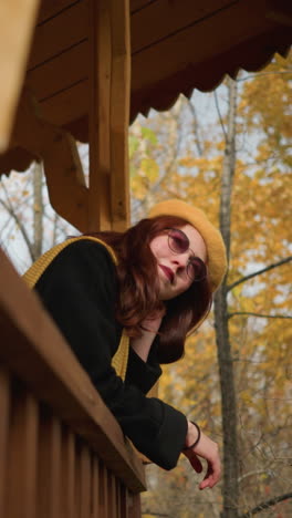 una joven tocando juguetonamente su cabello mientras descansa su mano en la cuña del mirador, rodeada de árboles con hojas que se balancean suavemente
