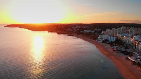 Tolle-Luftaufnahme,-Herauszoomen-Aus-Der-Sonne,-In-Der-Skyline-Der-Stadt-Armação-De-Pêra-Bei-Sonnenuntergang