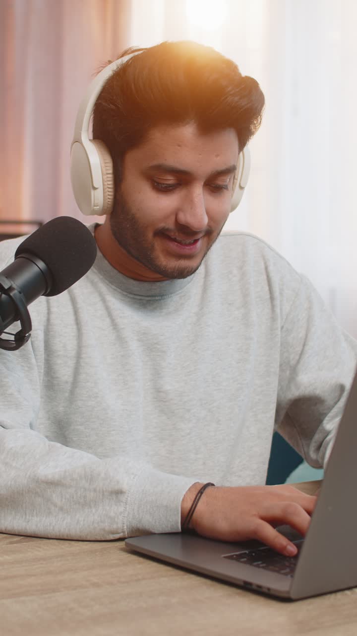 Hindu man using laptop recording vlog and conducting online stream while sitting at table at home