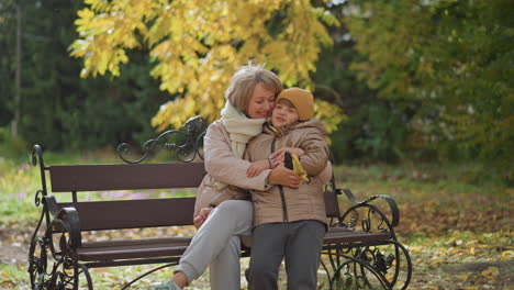 lovely moment as instructor hugs child warmly on park bench amid autumn leaves swaying gently in breeze, surrounded by golden foliage and crisp seasonal ambience capturing affectionate bond