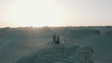 group of friends in casual wear enjoying vacation, climb on the edge of cliff in desert