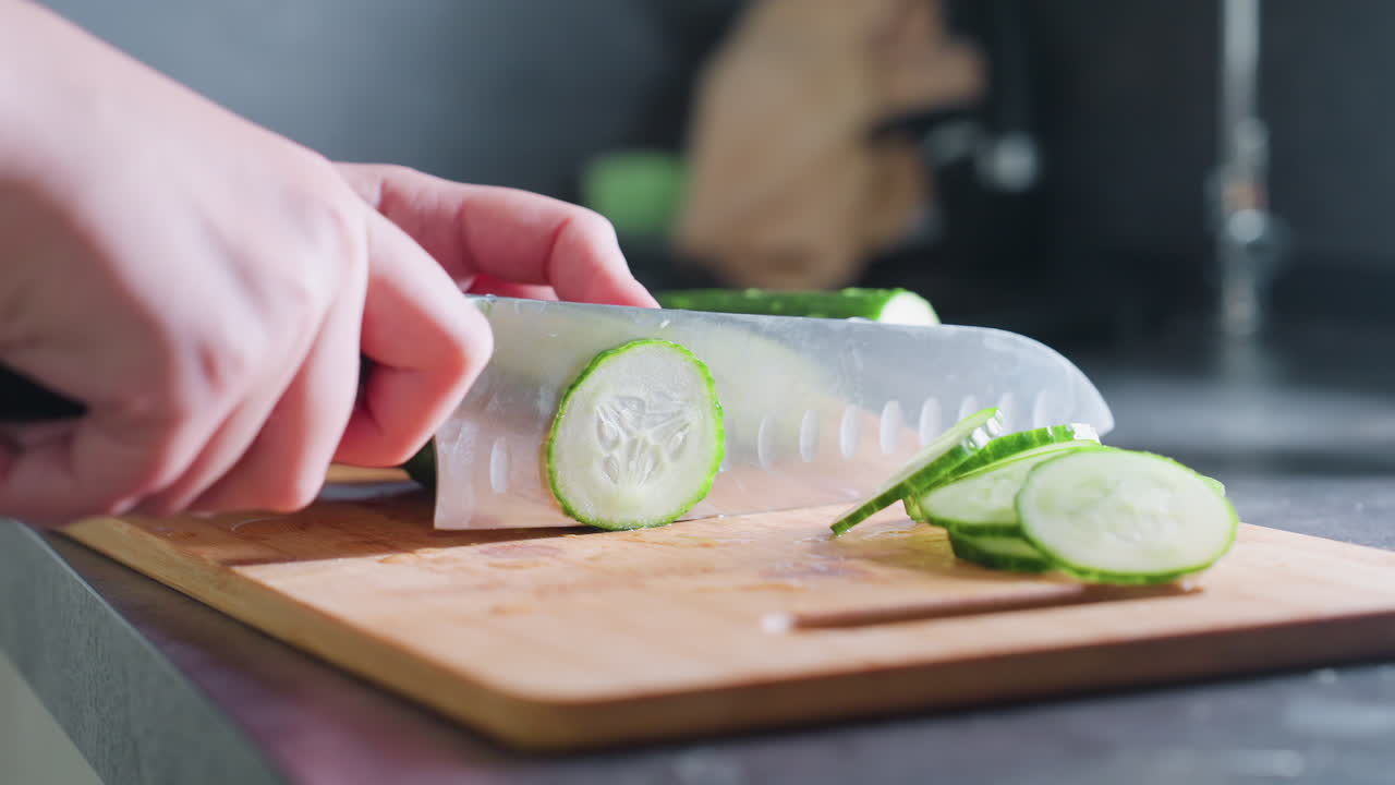 Close-up view of hand slicing cucumber into smaller pieces on wooden cutting board, focus on precision and kitchen action, perfect for food preparation and healthy cooking scenes