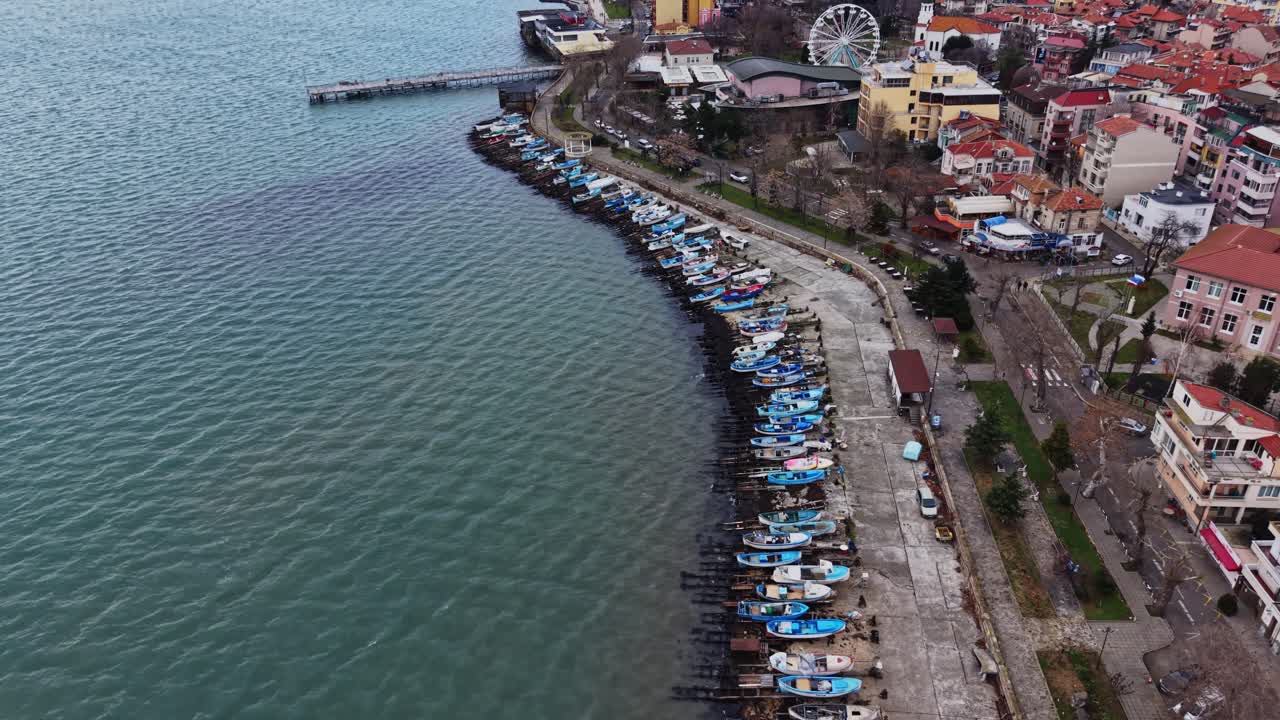 Boats lined up along the shoreline near a town in the evening