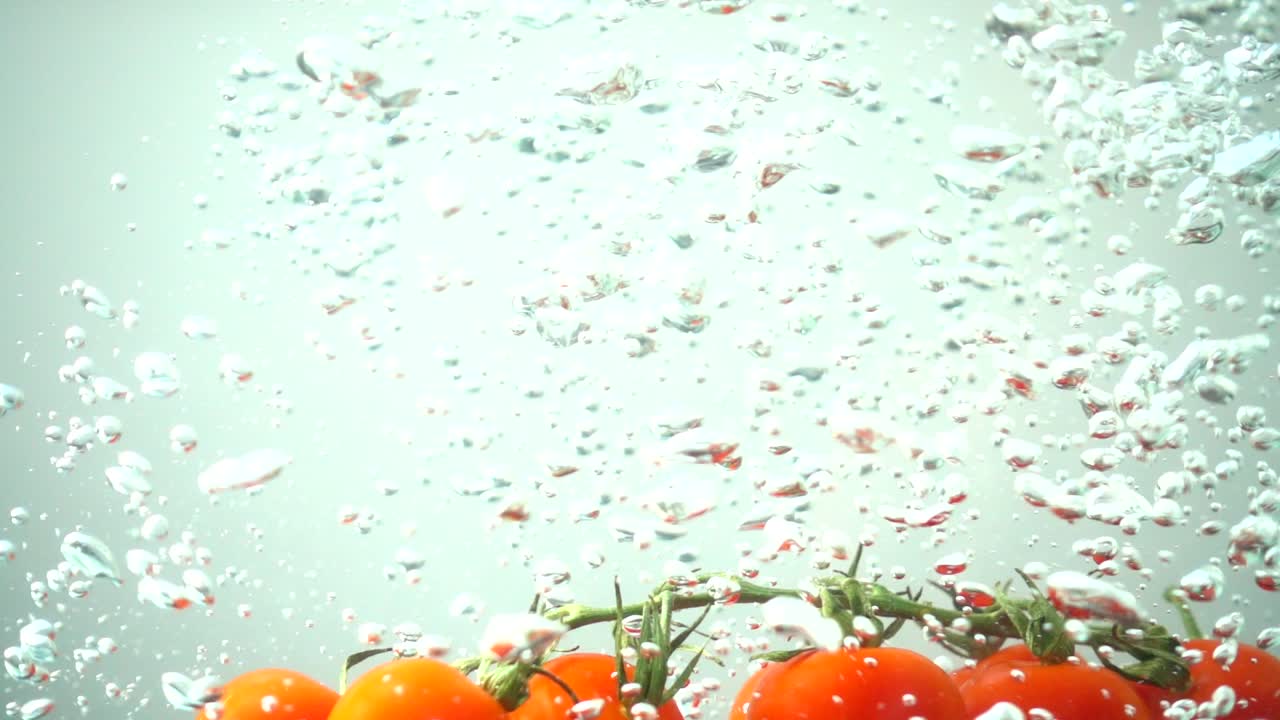 Fallende Kirschtomaten im Wasser. Zeitlupe.