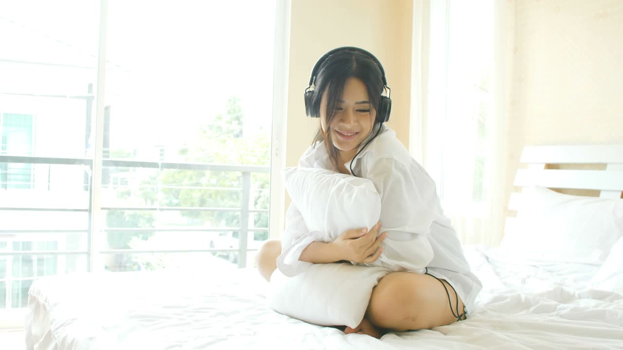 젊은 아시아 여성들이 침대에서 음악을 듣고 있습니다.