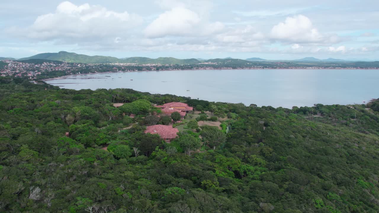 Bird's eye view of a tourist villa in B&uacute;zios, Brazil hidden in a lush and dense jungle, clouds in the background