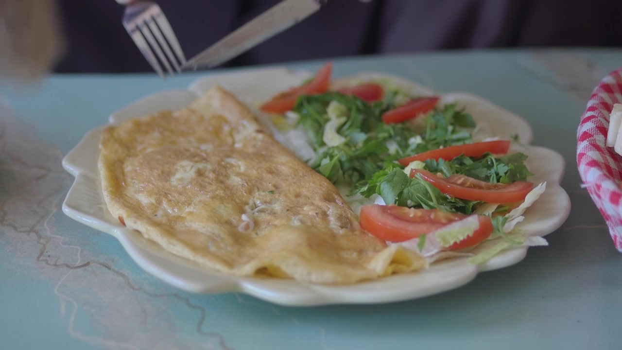 Person Cutting an Omelet with a Side Salad on a Plate