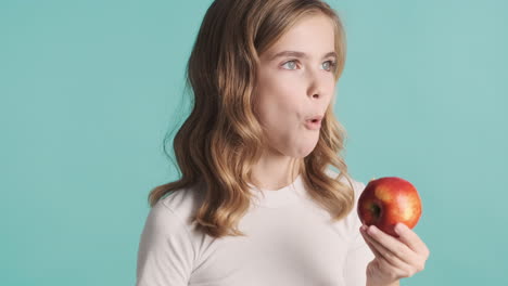 una adolescente caucásica en pijama comiendo una manzana y sonriendo.