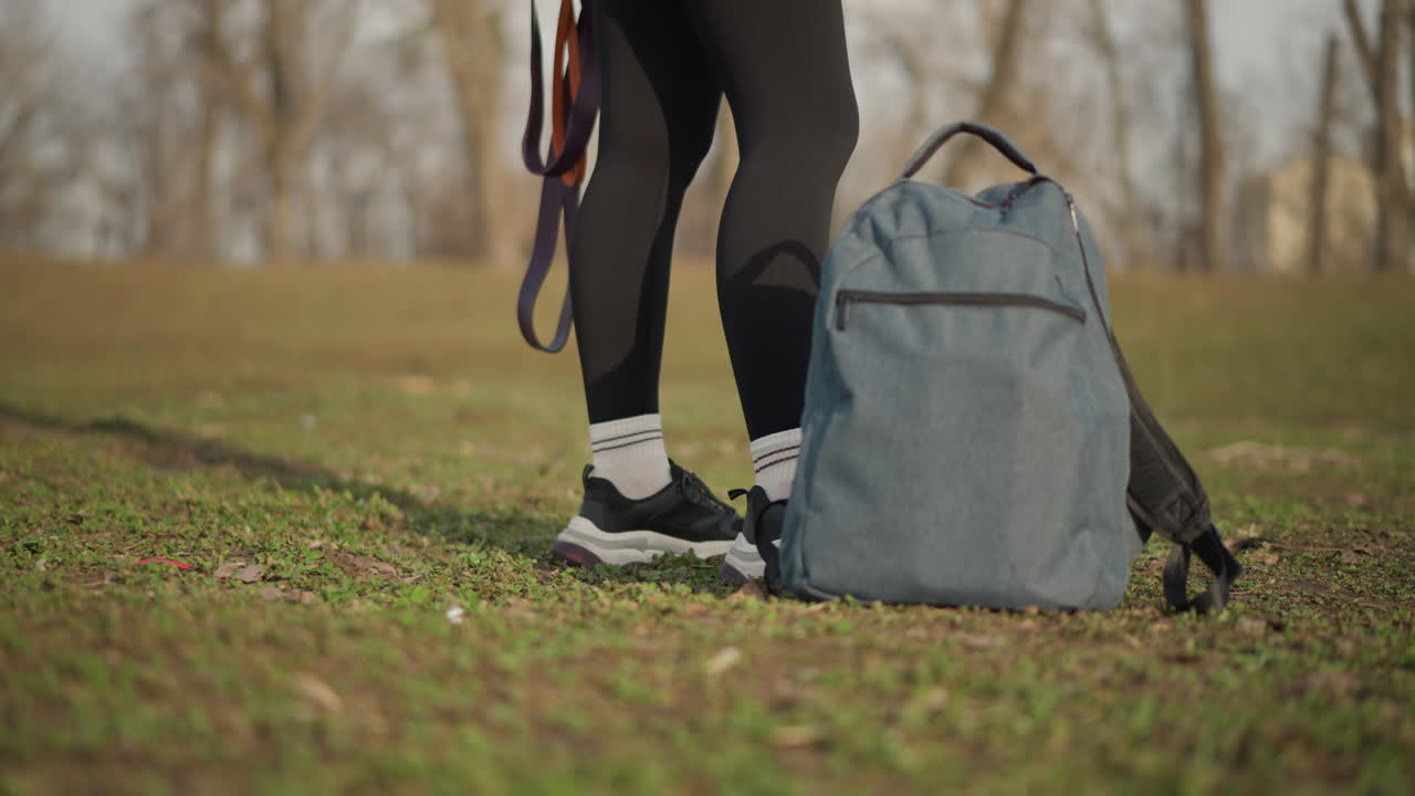 Asian Woman CloseUp On Feet And Lower Legs Walking In Park, Sneakers Planting On Grass Beside Backpack And Leashes, Steady Cadence And Textured Ground Highlight Movement And Practical Gear