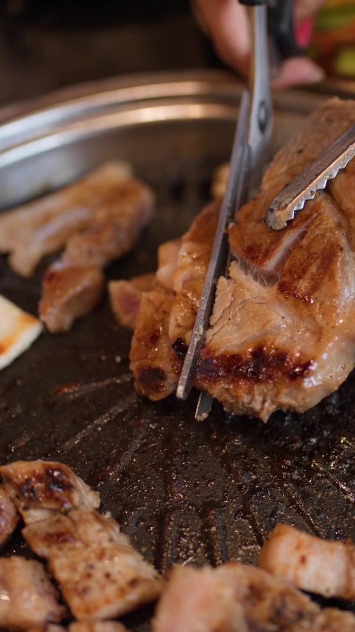 Close-up gunting memotong daging babi yang diasinkan di atas panggangan logam panas dengan pencahayaan alami