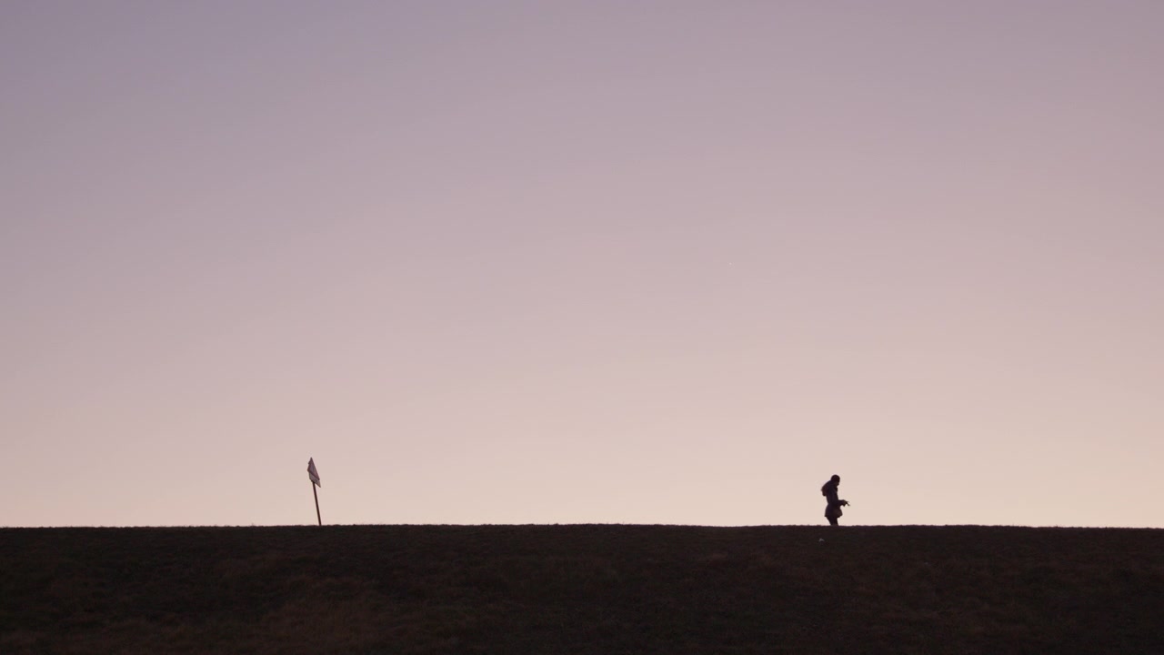 Donna in silhouette che cammina su una collina al tramonto.