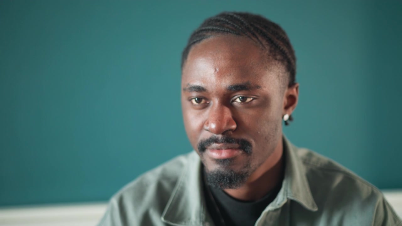Black man home consultation patient portrait, closeup of thoughtful expressions during remote checkup and inperson nursing followup teal wall background, soft natural lighting, subtle smile, attentive