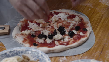 El-Chef-Encabeza-La-Pizza-Napolitana-Con-Aceitunas-Negras,-Sobre-Una-Mesa-De-Madera