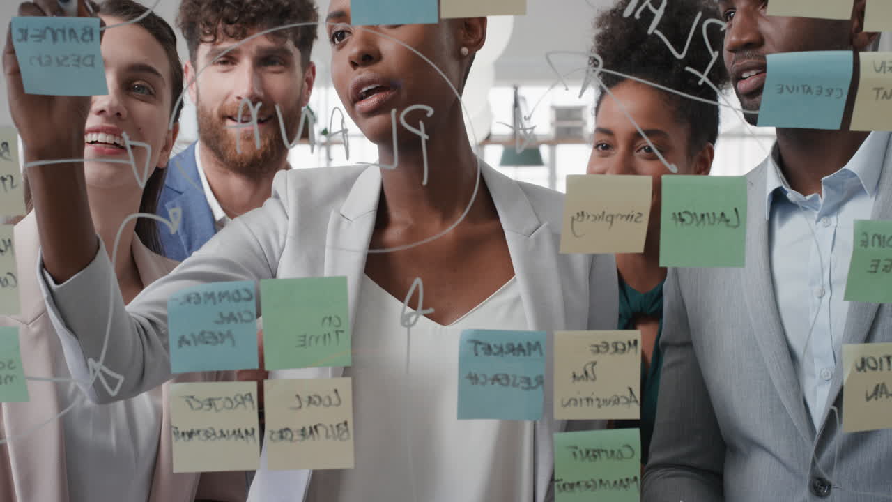 기업 사업가 들 은 스티키 노트 를 사용 하여 문제 해결 전략 을 유리 화이트 보드 에 작성 한다