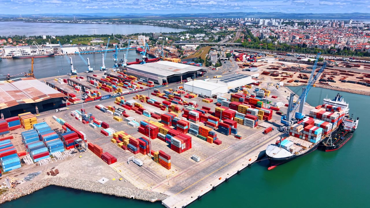 Burgas, Bulgaria, 10 aprile 2026: Vista aerea di container per spedizioni e gru a portale. Fitte pile di container rossi, blu e gialli con nave all'ormeggio e la città sullo sfondo.