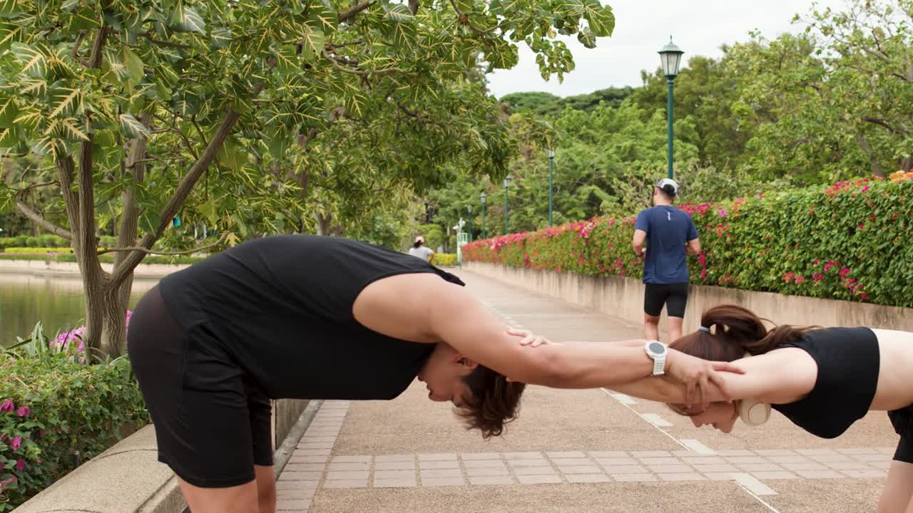 Hombre y mujer tailandeses atléticos realizan estiramientos asistidos de espalda e isquiotibiales durante un entrenamiento al aire libre