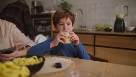 niño bebiendo batido en la mesa de la cocina
