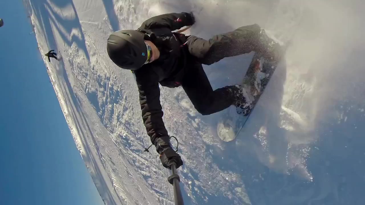 Front view of a snowboarder going down the mountain with a selfie stick and nearly falling. Jasna, Slovakia.
