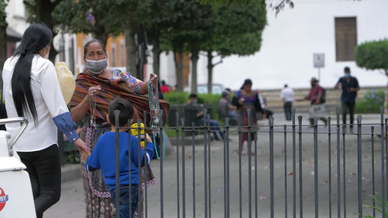 Antigua Guatemala woman wears traditional colorful handmade dress, offering necklaces and souvenirs to tourists, wearing face mask due to recent Covid-19 pandemic - Slow motion