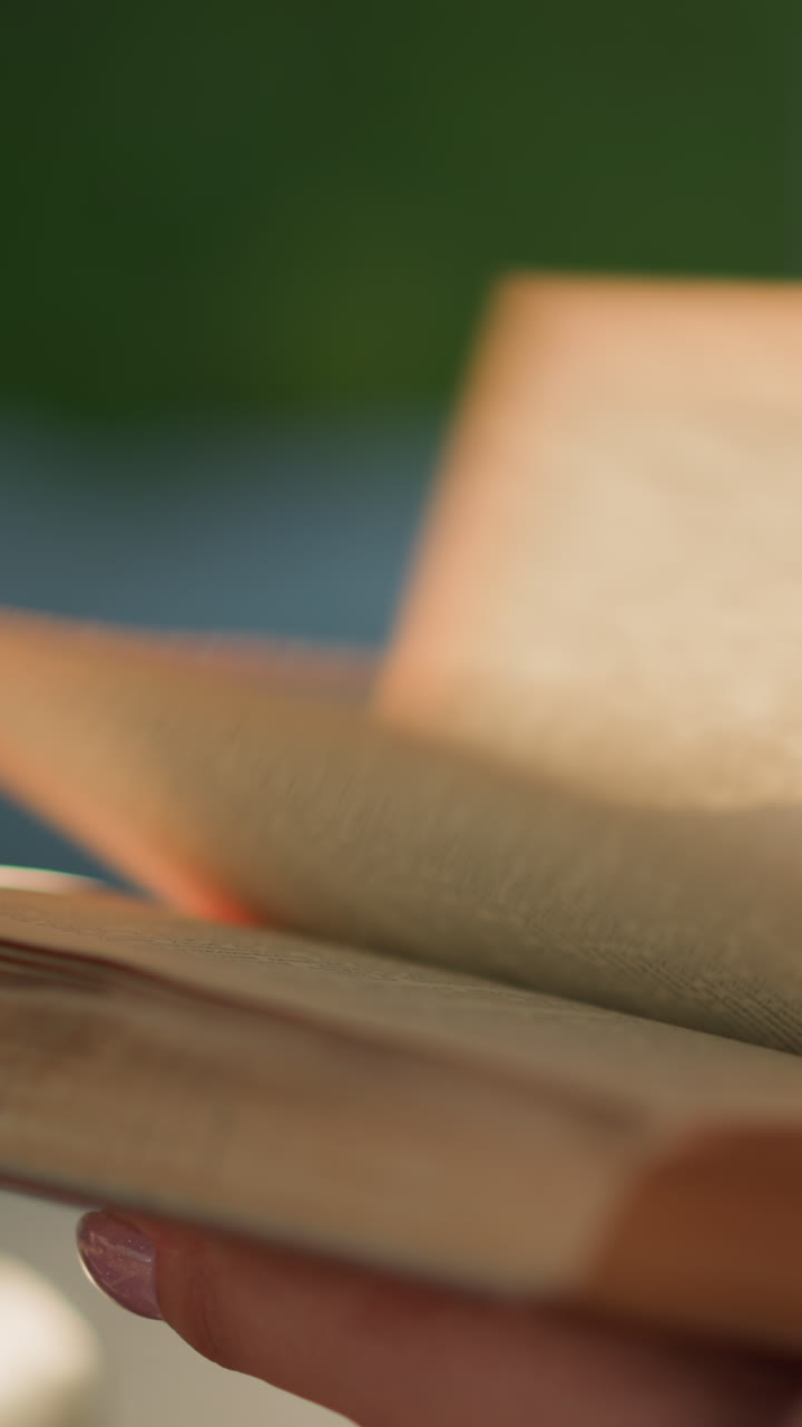 primer plano de un libro individual mientras las páginas se voltean rápidamente hacia la derecha, la luz del sol arroja un brillo suave en las páginas mientras que el fondo, con vegetación, está borroso