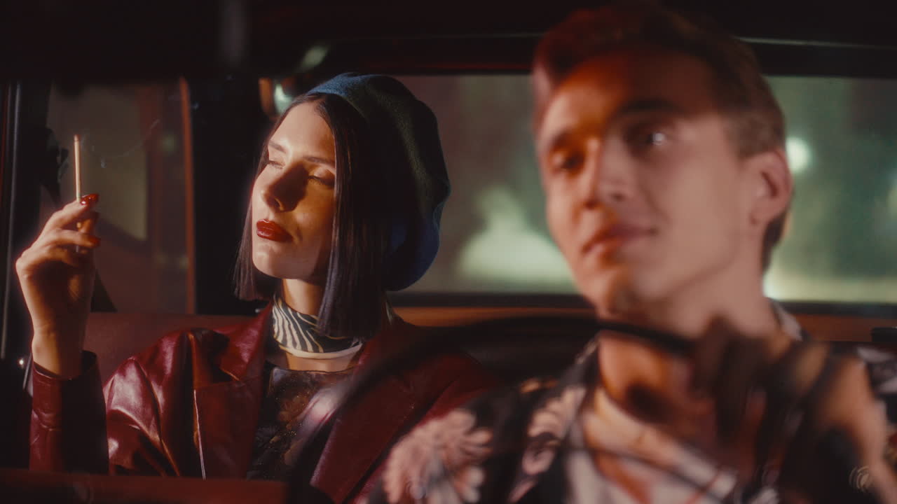 Attractive Woman Smoking in Passenger Seat and Talking to Man Driving at Night